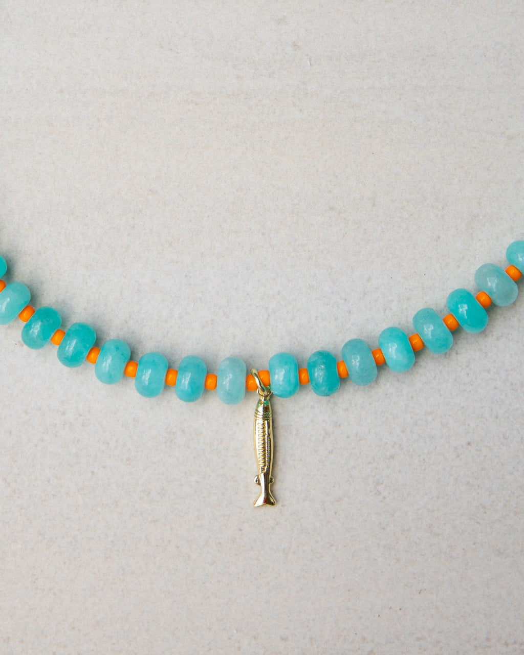 Necklace with blue beads and a gold fish charm on a light gray background