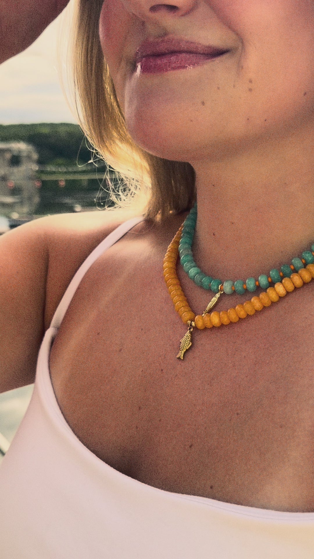 Girl with tan lines wearing stacked beaded necklaces with gold fish charms